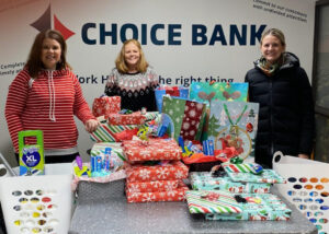three women stand behind a table with Christmas gifts